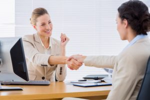 Smartly dressed young women shaking hands in a business meeting at office desk